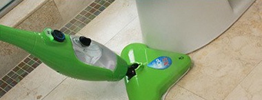 Steam cleaning the floor against the edge of a toilet